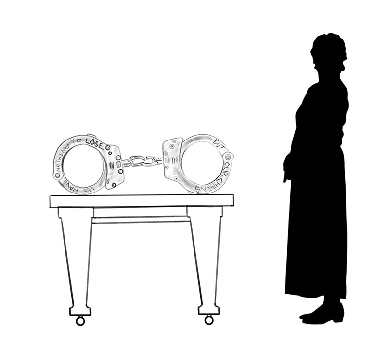 image of two individuals standing on either side of a large scale sculpture of handcuffs