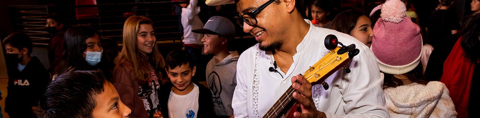 A mexican man shows a guitar to a young bow in front of a crowd.