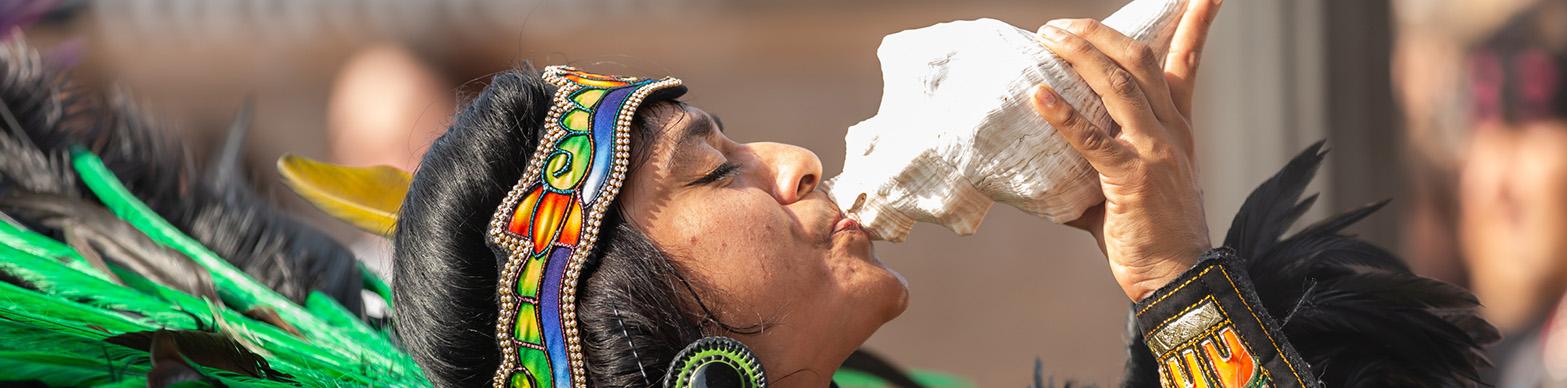 Individual in traditional dress playing a conch shell