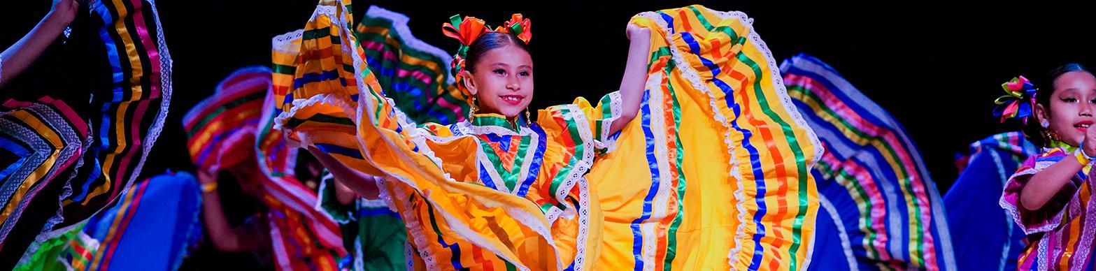 A young girl dances on stage in traditional mesican foklorico attire