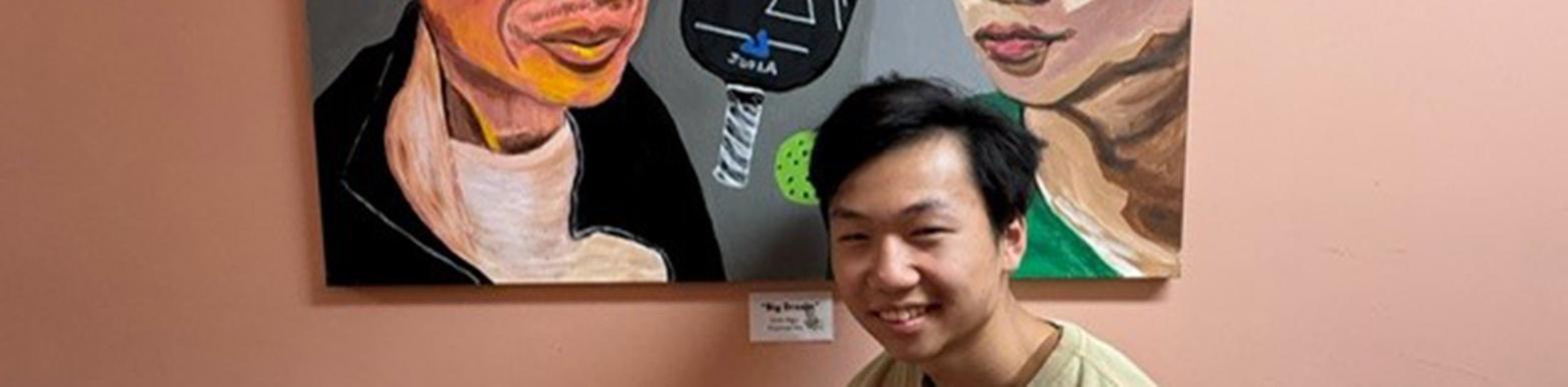 An Asian man poses in front of a painted self portrait