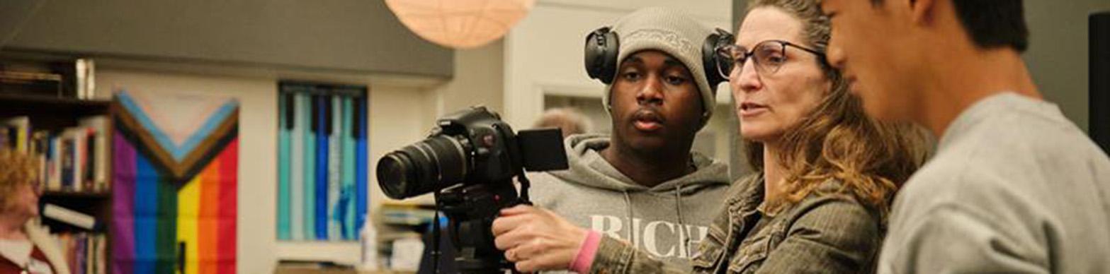 One Black student and one asian student look on as a white instructure demos a camera