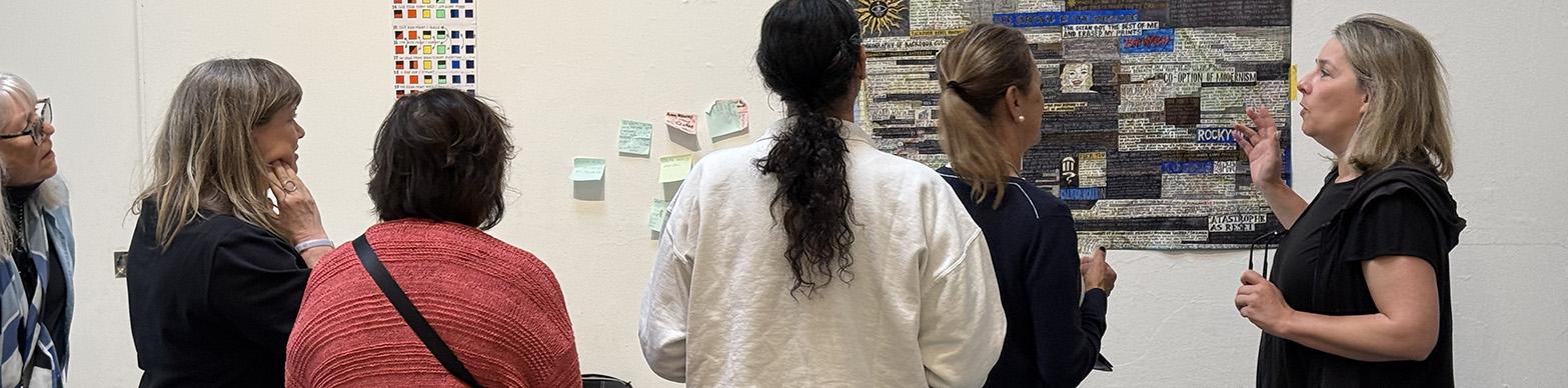 Image of individuals on a tour, looking at a work of abstract art hung on a white wall