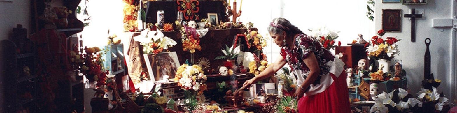 An elderly latina woman interacts with an elaborate ofrenda