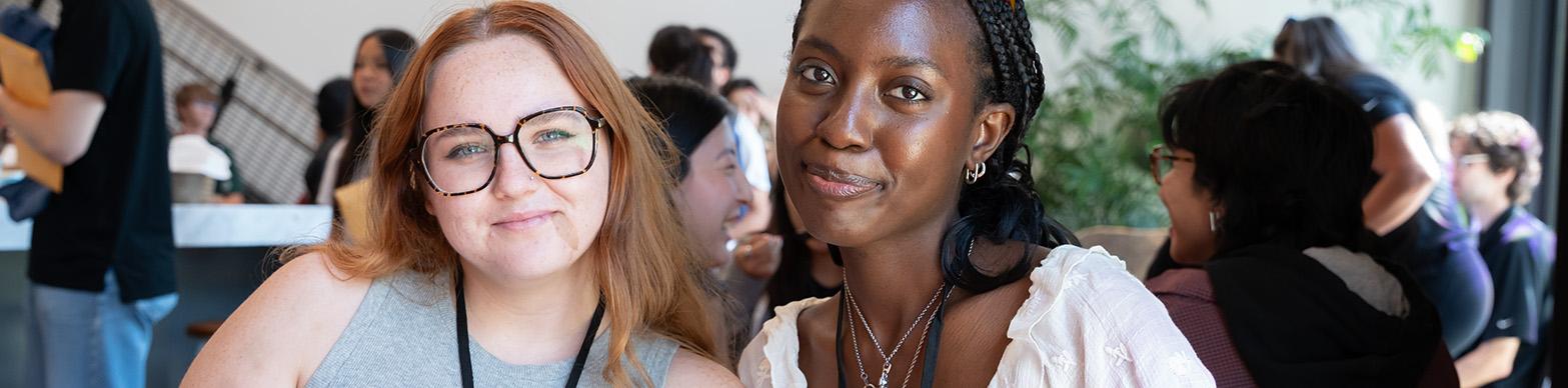 Two young women pose for a photo while sitting at a table