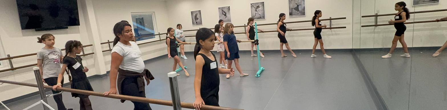 nine young girls perform barre exercises