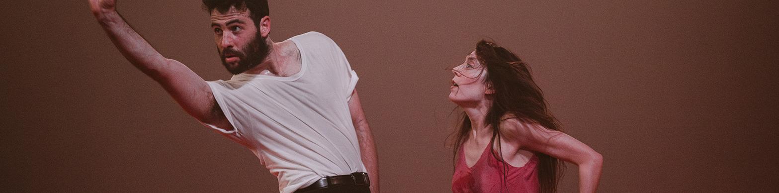 Two dancers pose in front of a brown background