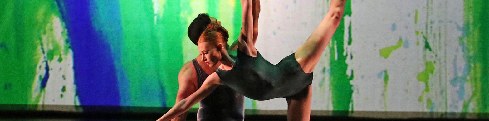 Two ballet dancers dance in front of a green and blue background