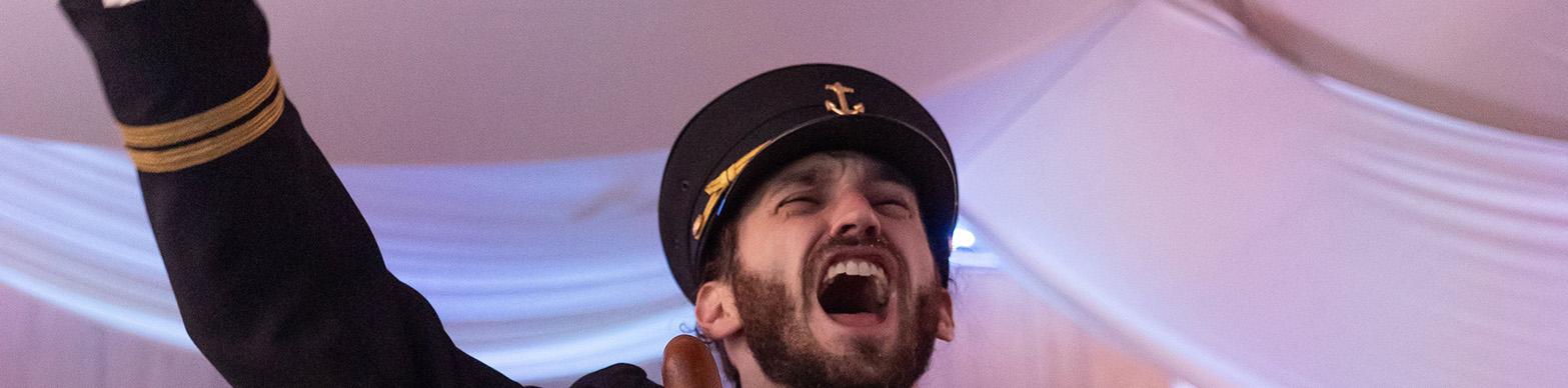 Man in captains uniform holds hand up on stage