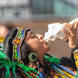 Individual in traditional dress playing a conch shell