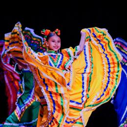A young girl dances on stage in traditional mesican foklorico attire