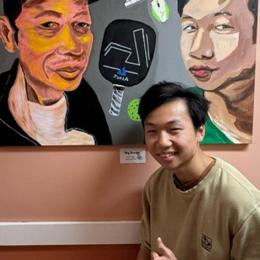 An Asian man poses in front of a painted self portrait