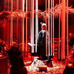 Individuals singing on stage surrounded by read curtains